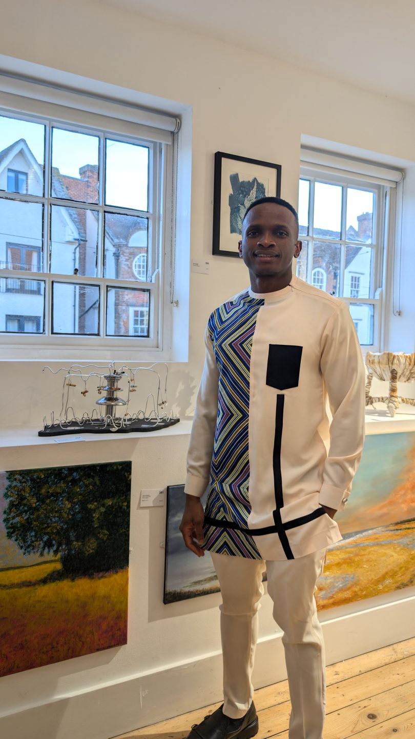 Favour Agumadu standing next to the his work “Death’s Goblet” at the Letchworth Open Exhibition 2024 in UK.